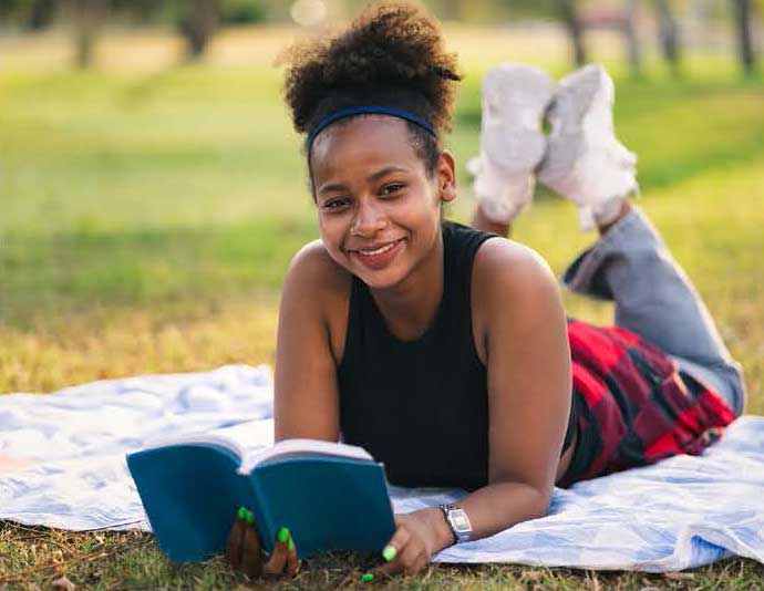 student laying outside reading a book
